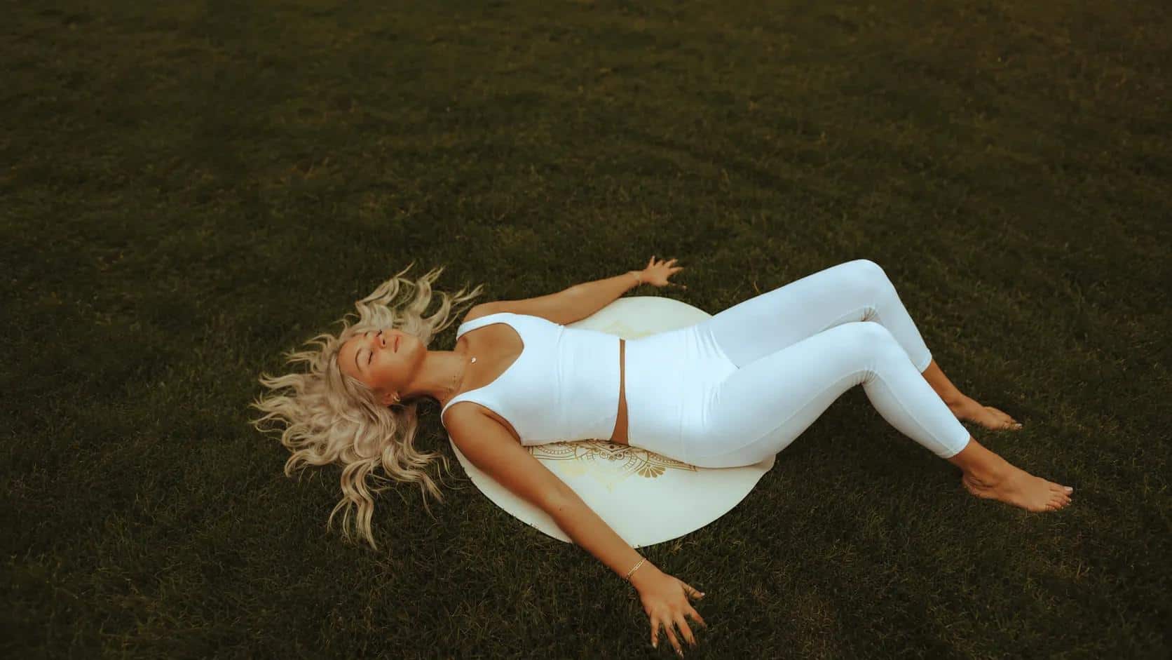Ansar Benboudjemaa, hypnothérapeute, allongée dans l'herbe au lever du jour, dans une tenue claire, posture de détente